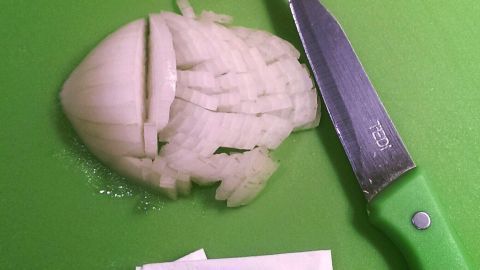Eine Zwiebel liegt auf einem grünen Schneidebrett, neben einem Messer, während die geschälte Wimper bei der Zubereitung von Speisen ist.