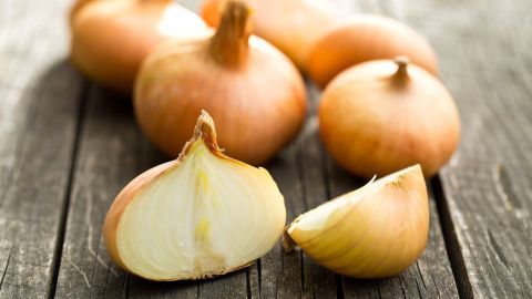 Schnelle Hilfe bei einem Wespen- oder Bienenstich mit einer halben rohen Zwiebel. Zwiebeln liegen auf einem Holzuntergrund, einige sind ganz, andere sind halbiert und zeigen das Innere.