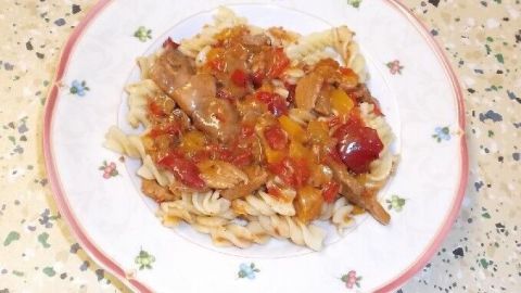 Ein Teller mit spiralförmigen Nudeln, bedeckt mit Gulasch aus Gyros, serviert auf einer dekorierten Unterlage.
