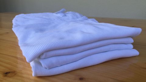 Sauber gefaltete alte Baumwollunterhemden liegen ordentlich auf einem Holztisch, bereit für die Wiederverwendung oder weitere Nutzung.