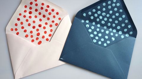 Leuchtend gepunktete Briefumschläge liegen nebeneinander, einer in Rosa mit roten Punkten, der andere in Blau mit weißen Punkten.