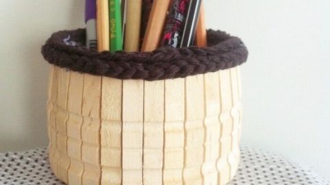 Ein Utensilienbehälter aus Holz mit bunten Stiften wird auf einem gepunkteten Tisch präsentiert, umgeben von Wäscheklammern.