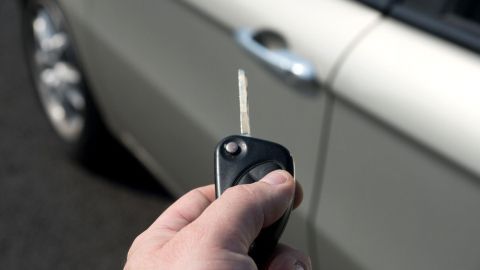 Ein Autoschlüssel wird in der Hand gehalten, während er darauf abzielt, ein Auto zu entriegeln, das in der Nähe steht.