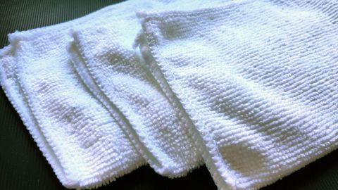 Mehrere weiße Microfasertücher liegen übereinander auf einer dunklen Unterlage, bereit zur sanften Gesichtsreinigung.