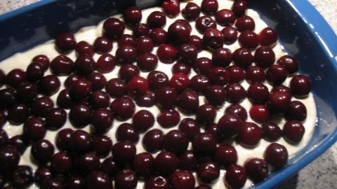 Ein Kirsch-Quark-Auflauf liegt in einer blauen Auflaufform, gefüllt mit einer Schicht Quark und bedeckt von vielen Kirschen.