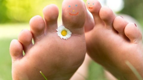 Barfußfüße mit einer blühenden Blume liegen auf grünem Gras und strahlen Freude und Gesundheit aus, ideal gegen Fußpilz.