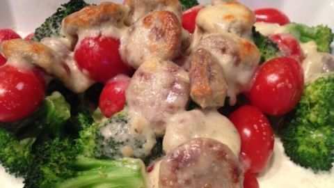 Ein Brokkoli-Tomaten-Bratwurst-Auflauf mit schmelzendem Käse liegt appetitlich angerichtet in einer weißen Auflaufform.
