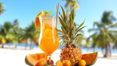 Ein klassischer Cocktail steht auf einem Holztisch, umgeben von frischen Früchten und einer sonnigen Strandkulisse.