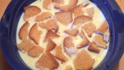 Eine blau-weiße Schale enthält eine cremige Buttermilchkaltschale, belegt mit knusprigen Brotwürfeln, auf einem Holzuntergrund.