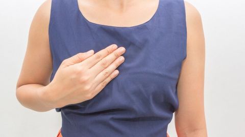 Eine Person hält ihre Hand auf die Brust, um Beschwerden durch lästiges Sodbrennen zu zeigen, in einem neutralen Umfeld.