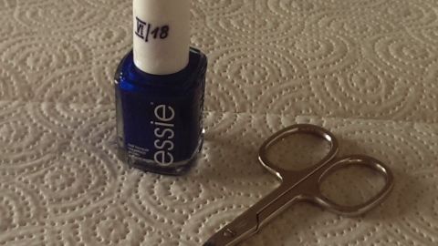 Ein blauer Nagellack steht neben einer kleinen Schere auf einer Küchenarbeitsfläche mit Pappetuch.