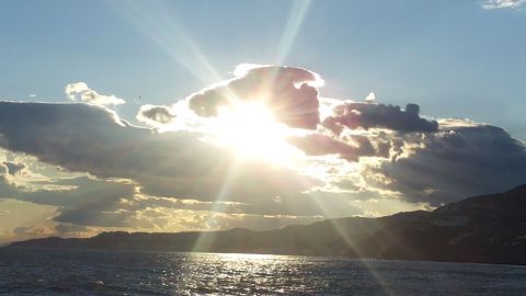 Ein strahlender Sonnenuntergang reflektiert auf dem Wasser, während Wolken den Himmel umgeben und eine ruhige Atmosphäre schaffen.