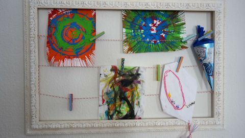 Ein leerer Bilderrahmen dient als kleine Kunstgalerie, in der bunte Kinderzeichnungen auf einer Schnur hängen.