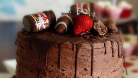 Ein Schokokuchen ist kunstvoll dekoriert mit Nutellagläsern und einer Erdbeere, auf einem eleganten Tortenteller platziert.