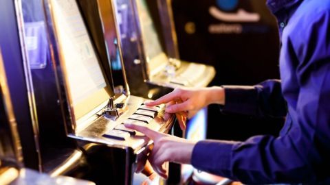 Ein Spieler sitzt an einem Spielautomaten und drückt die Tasten, während er darauf wartet, zu gewinnen.