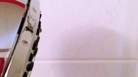 Ein Duschkopf wird in Richtung der Glaswände gehalten, um sie schnell sauber und trocken zu machen. Die Wände sind weiß fliesenverkleidet.