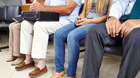 Mehrere Menschen sitzen in einem Warteraum, nervös ihre Beine bewegend, während sie die Wartezeit sinnvoll überbrücken.