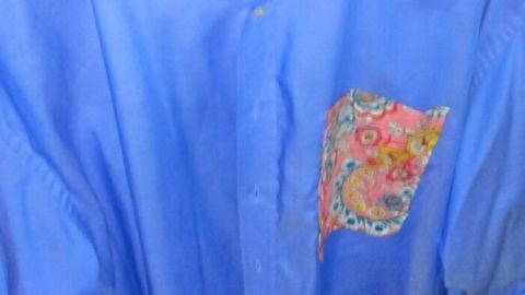 Ein blauer Hemd hängt an einem Kleiderbügel, mit bunten floralem Kragen und kleiner Brusttasche, bereit zur Wiederverwendung.