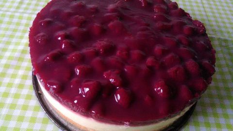 Eine Himbeer-Schmand-Torte liegt auf einem karierten Tisch, glänzend mit einer fruchtigen Schicht und frischen Himbeeren.
