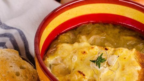 Eine üppige Zwiebelsuppe mit geschmolzenem Käse in einer bunten Schüssel, umgeben von frischen Zwiebeln und Brot.