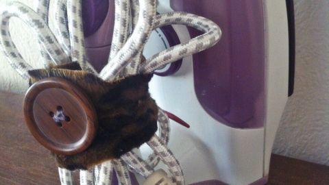 Ein Bügeleisen steht auf einem Tisch, während sein Kabel ordentlich mit einem Knopf zusammengewickelt ist.