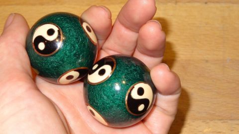 Eine Hand hält zwei grüne Klangkugeln mit Yin-Yang-Symbolen, die zur Meditationsübung für mehr Wohlbefinden genutzt werden.
