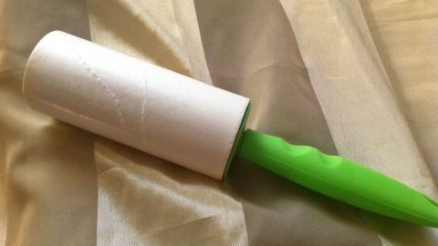 Eine Fusselrolle mit einem grünen Griff liegt auf einem gestreiften Stoff. Sie ist bereit, Fussel und Haare zu entfernen.