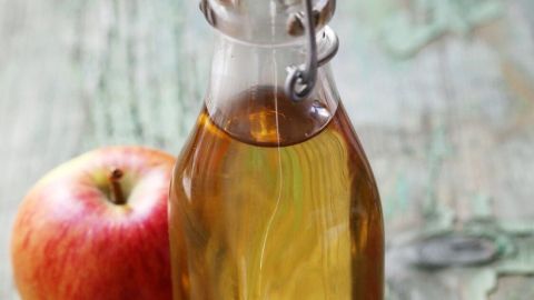 Eine Glasflasche mit Apfelessig steht neben einem frischen roten Apfel auf einem rustic Holzuntergrund.