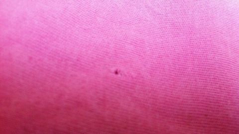 Ein kleiner schwarzer Punkt auf pinkem Stoff zeigt ein Loch in der Kleidung, das möglicherweise Schäden verursacht.