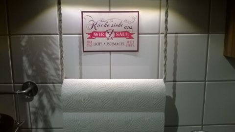Ein Rollenhalter für Zewa mit einer dekorativen Wandtafel darüber in einer modernen Küche. Leicht beleuchtet bietet er praktischen Nutzen.