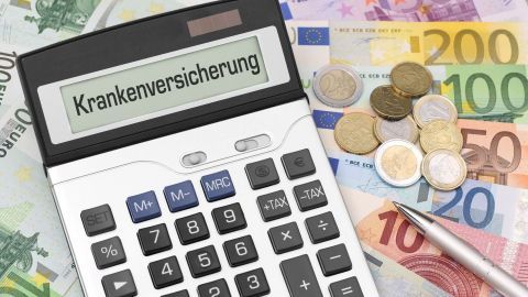 Ein Taschenrechner zeigt "Krankenversicherung" an, umgeben von Euro-Münzen und -Scheinen, die finanzielle Aspekte verdeutlichen.