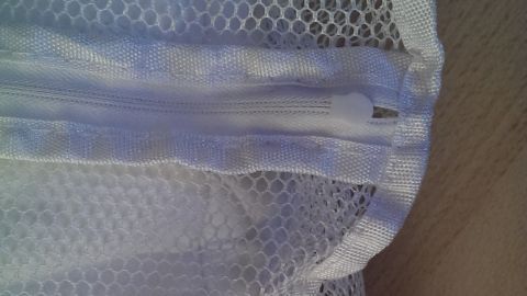 Ein Wäschenetz liegt mit dem Verschluss nach oben auf einem Tisch, bereit zum Einsatz, um Kleidung beim Waschen zu schützen.
