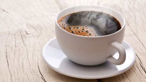 Eine Tasse Kaffee steht auf einem Holztisch, dampfend und aromatisch, was den Koffeinkonsum symbolisiert.