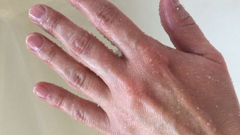 Hände pflegen mit einem selbst gemachten Peeling aus Olivenöl und Zucker. Eine Hand, die sich in einer Rührschüssel mit Peelingprodukt befindet, wird sanft behandelt, um abgestorbene Haut zu entfernen.