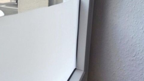 Eine selbstklebende Glasfolie wird an einem Fenster angebracht, während das Zimmer hell erleuchtet ist und ein Kabel sichtbar ist.