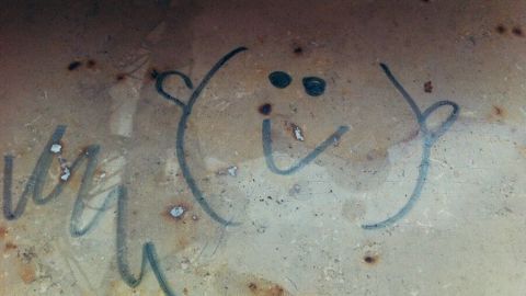 Ein brauner Untergrund zeigt einen Edding-Schriftzug und ein Smiley, das Flecken auf der Oberfläche hinterlässt.