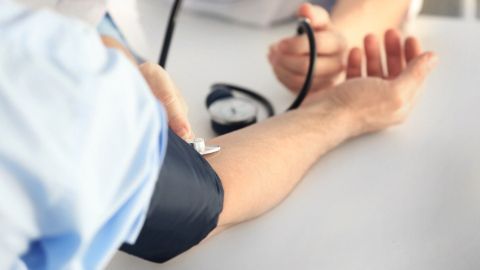 Ein Arzt misst den Blutdruck eines Patienten an einem Tisch, während ein Blutdruckmessgerät daneben liegt.