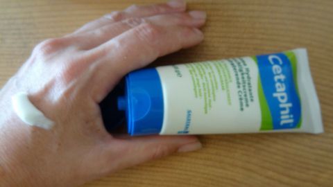 Eine Hand hält eine Tube Cetaphil-Creme, die auf empfindlicher Haut angewendet wird, zur Faltenreduzierung.