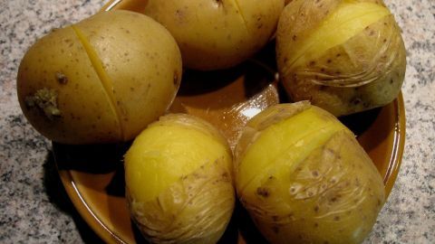 Ein Teller mit Pellkartoffeln, die teilweise geschält sind, liegt auf einer Marmorfläche und zeigt den einfachen Schälprozess.