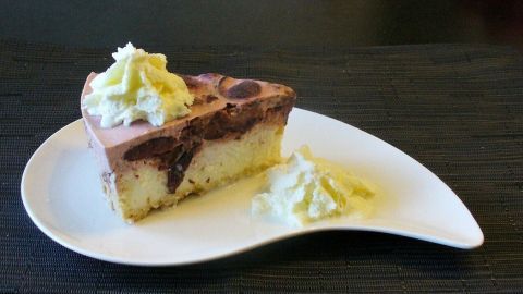 Ein Stück Käsekuchen mit einer cremigen Pflaumen-Frischkäsetopping ist auf einem eleganten weißen Teller angerichtet und umgeben von einem schlichten Schwarz.