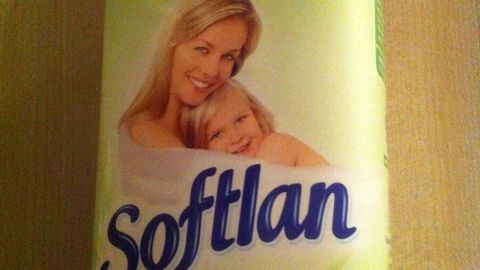 Eine Flasche Weichspüler steht vor einem hellen Hintergrund, während eine Mutter mit ihrem Kind lächelt und entspannt.