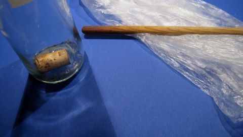 Eine Flasche mit einem Korken steht auf einem blauen Tisch, daneben liegt ein Holzstab und durchsichtige Folie.