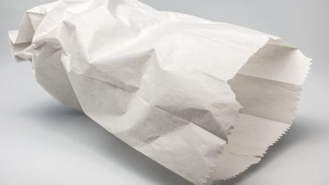 Ein zusammengeknüllter, weißer Papierbeutel liegt auf einem neutralen Hintergrund und wird zur sauberen Entsorgung von Tampons und Binden verwendet.