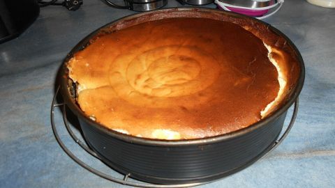 Ein Käsekuchen mit goldenem, leicht angebranntem Rand steht in einer Backform auf einer Küchenplatte, umgeben von Gerätschaften.