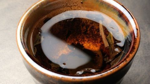 Ein schmaler Keramikbecher mit warmem, dunklem Getränk dampft leicht in einer ruhigen Umgebung.