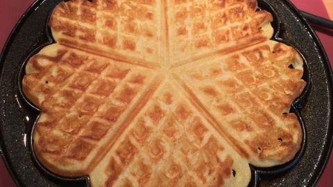 Buttermilchwaffeln in einer blütenförmigen Form, frisch gebacken und goldbraun, liegen auf einer warmen Waffelplatte.