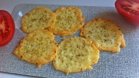 Käsechips liegen knusprig auf einer silbernen Platte, umgeben von frischen Tomatenscheiben. Ideal als Snack!
