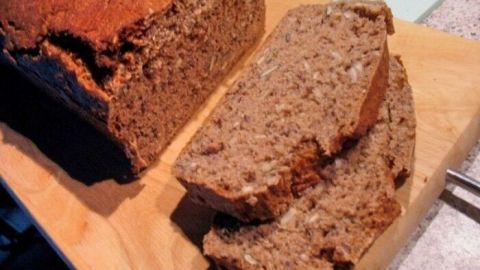 Ein frisch gebackenes, knuspriges Roggen-Mischbrot liegt auf einem Holzbrett, neben mehreren gleichmäßig geschnittenen Scheiben.