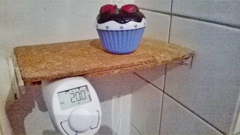 Ein Thermostat zeigt eine Temperatur von 20°C, während ein dekorativer Muffin auf einem kleinen Regal darüber steht.