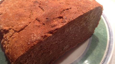 Ein rustikales Roggenvollkornbrot mit einer krustigen Oberfläche liegt auf einem grünen Teller, bereit zum Servieren.